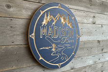 Decorative sign with 'Madison River' 'Ennis, MT, text and mountain fly fishing illustration on a wooden circle. Navy blue color